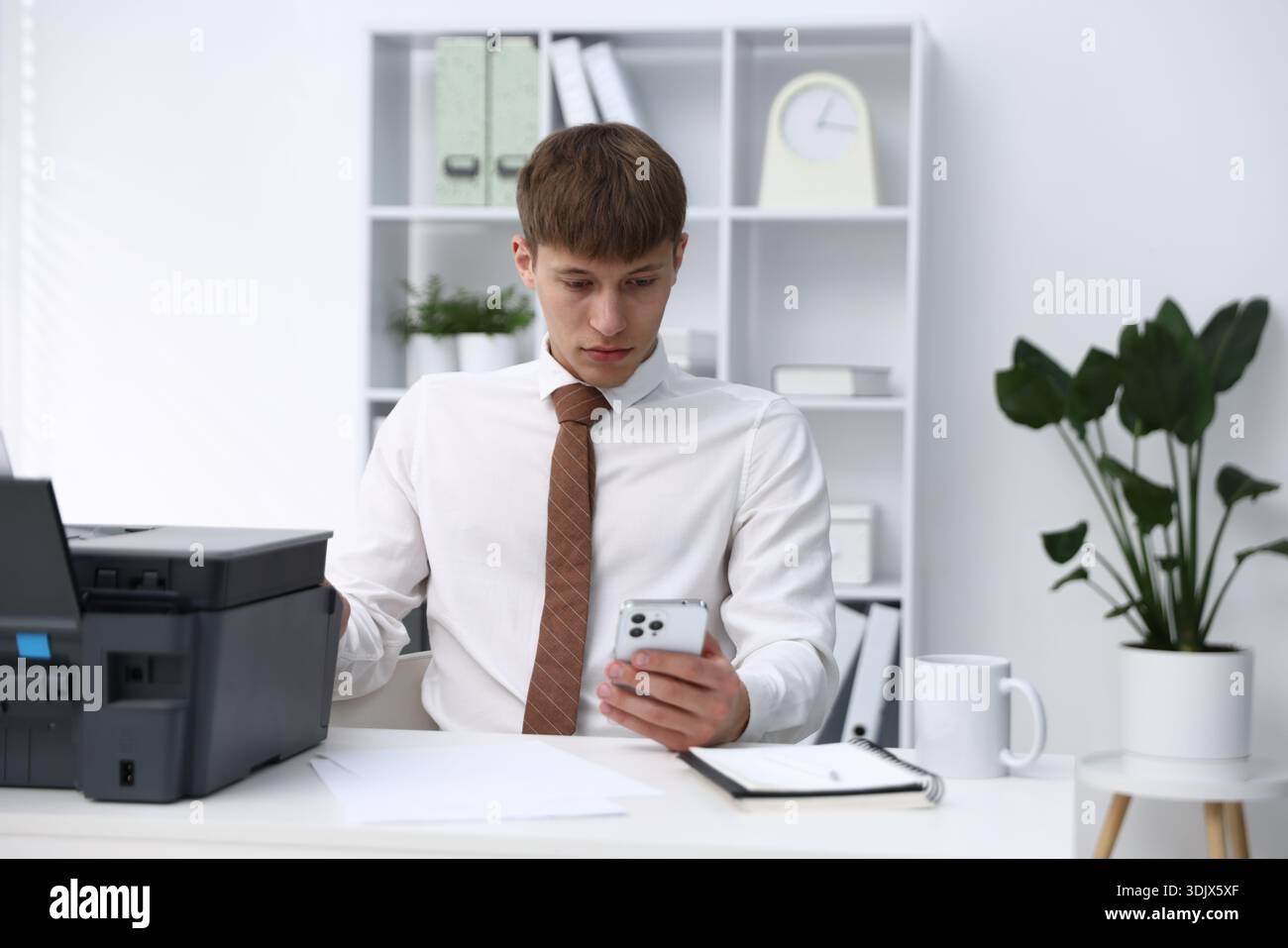 Man using printer and smartphone at white desk in office Stock Photo