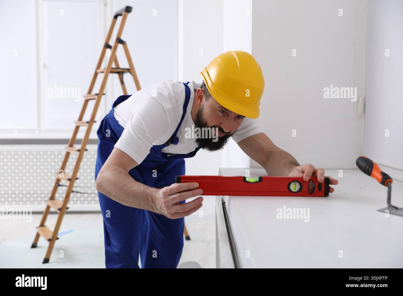 Worker measuring white dresser with building level indoors Stock Photo