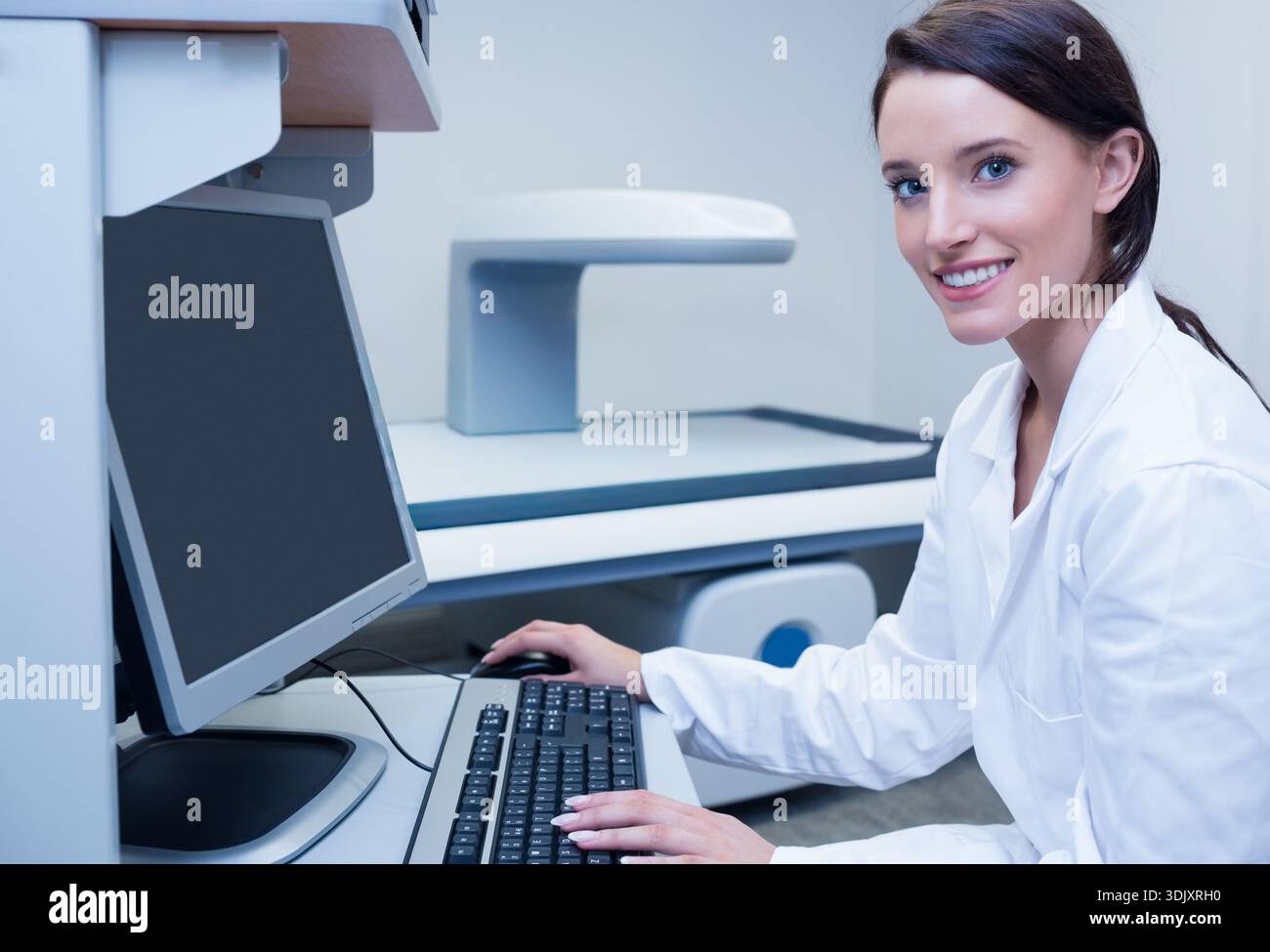 Clinical workstation is sitting at desk with widescreen monitor, keyboard and mouse in imaging room. Radiology, diagnostic, scanner, gantry, woman, cl Stock Photo