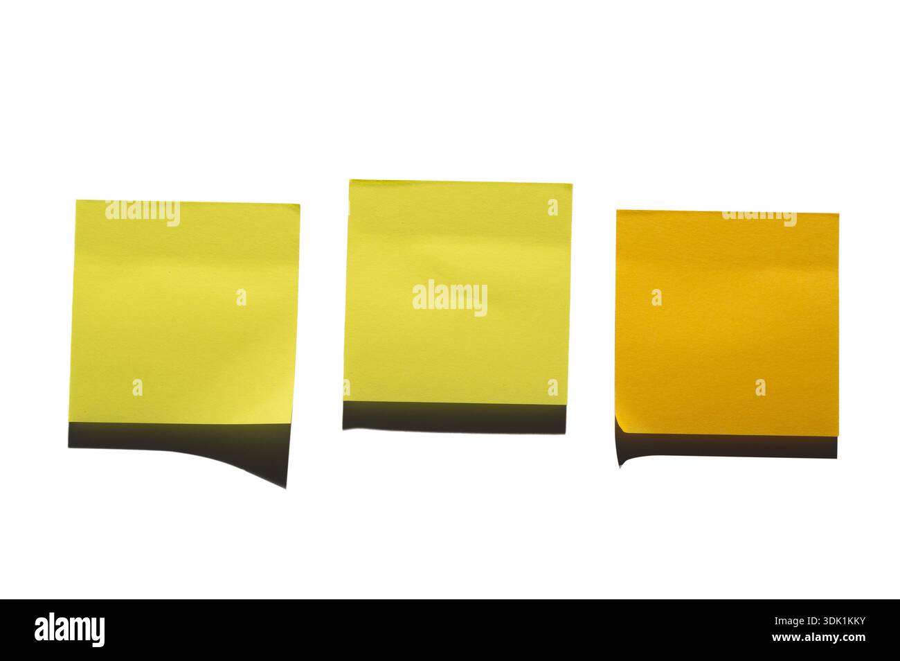 Three yellow sticky notes are arranged side by side against a white surface. The left note is a darker shade, while the two on the right are lighter. Stock Photo