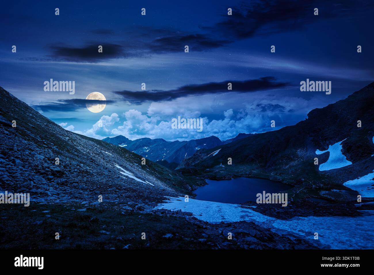 mountain lake in alpine summer landscape at night. beautiful view surrounded with clouds on a dark sky in full moon light. fresh water, snow and rocky Stock Photo