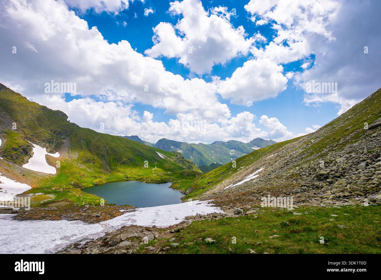 mountain lake in alpine summer landscape. beautiful view surrounded with transylvania alps and clouds on a blue sky. fresh water, snow and rocky slope Stock Photo