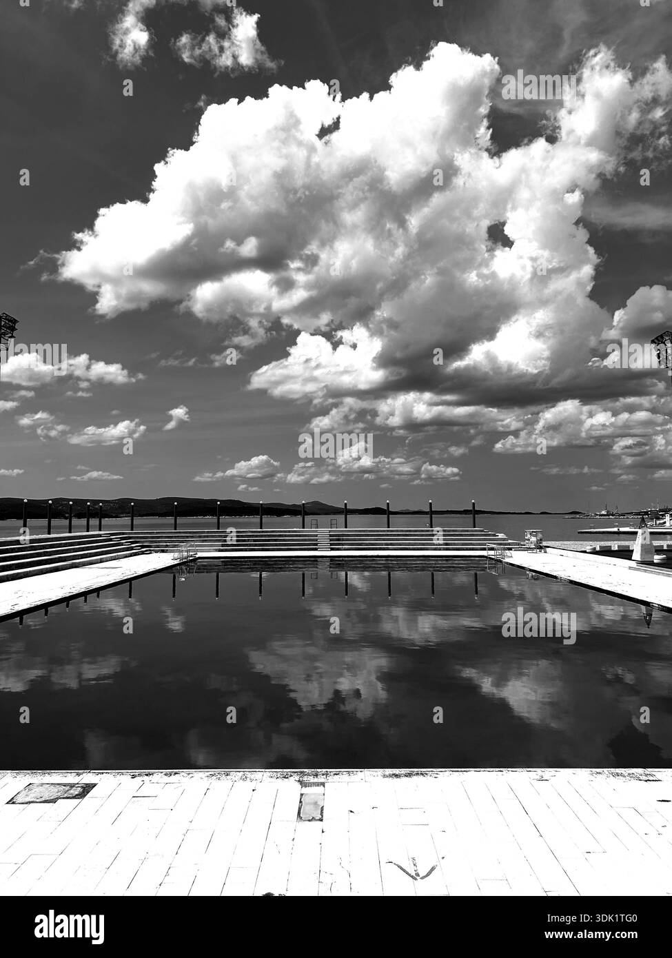 Outdoor public swimming pool overlooking the Adriatic Sea with blue summer sky an white fluffy clouds reflected in the water. - Smartphone Captured Stock Image