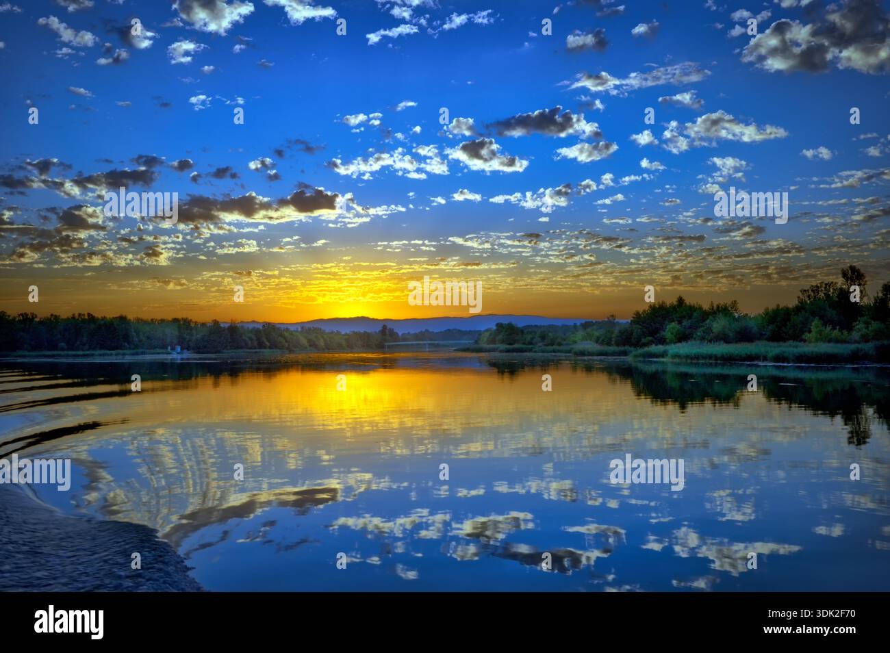 Rhone Flusslandschaft zur Blauen Stunde bis Sonnenaufgang. Wolkenglühen spiegelt sich im Wasser. Friedvolle Stimmung. Stock Photo