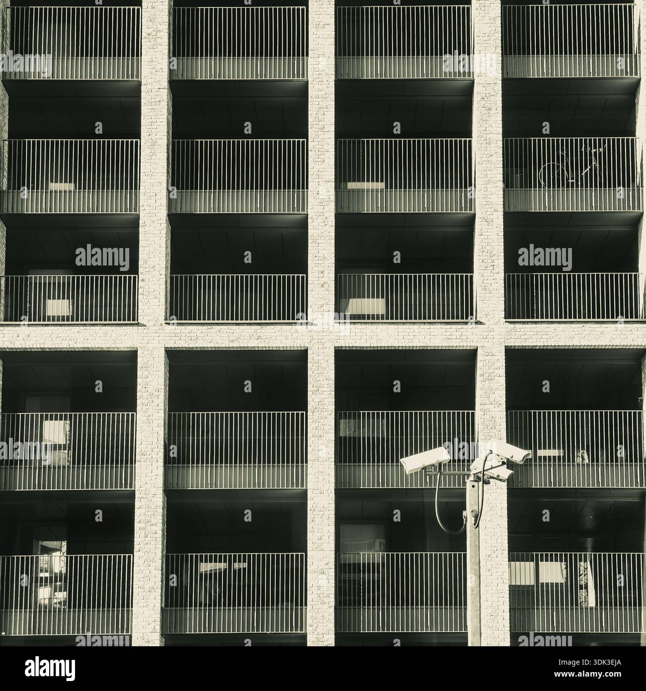 Monotone brutalist apartment block facade with uniform grid balconies, security cameras, and light poles creating geometric urban rhythm - Smartphone Captured Stock Image