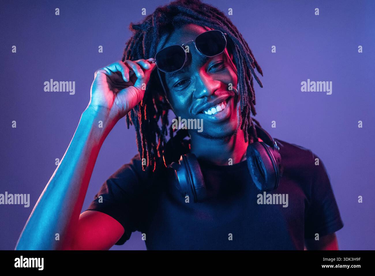Touching sunglasses, front view. African American guy is studio with neon lighting. Stock Photo