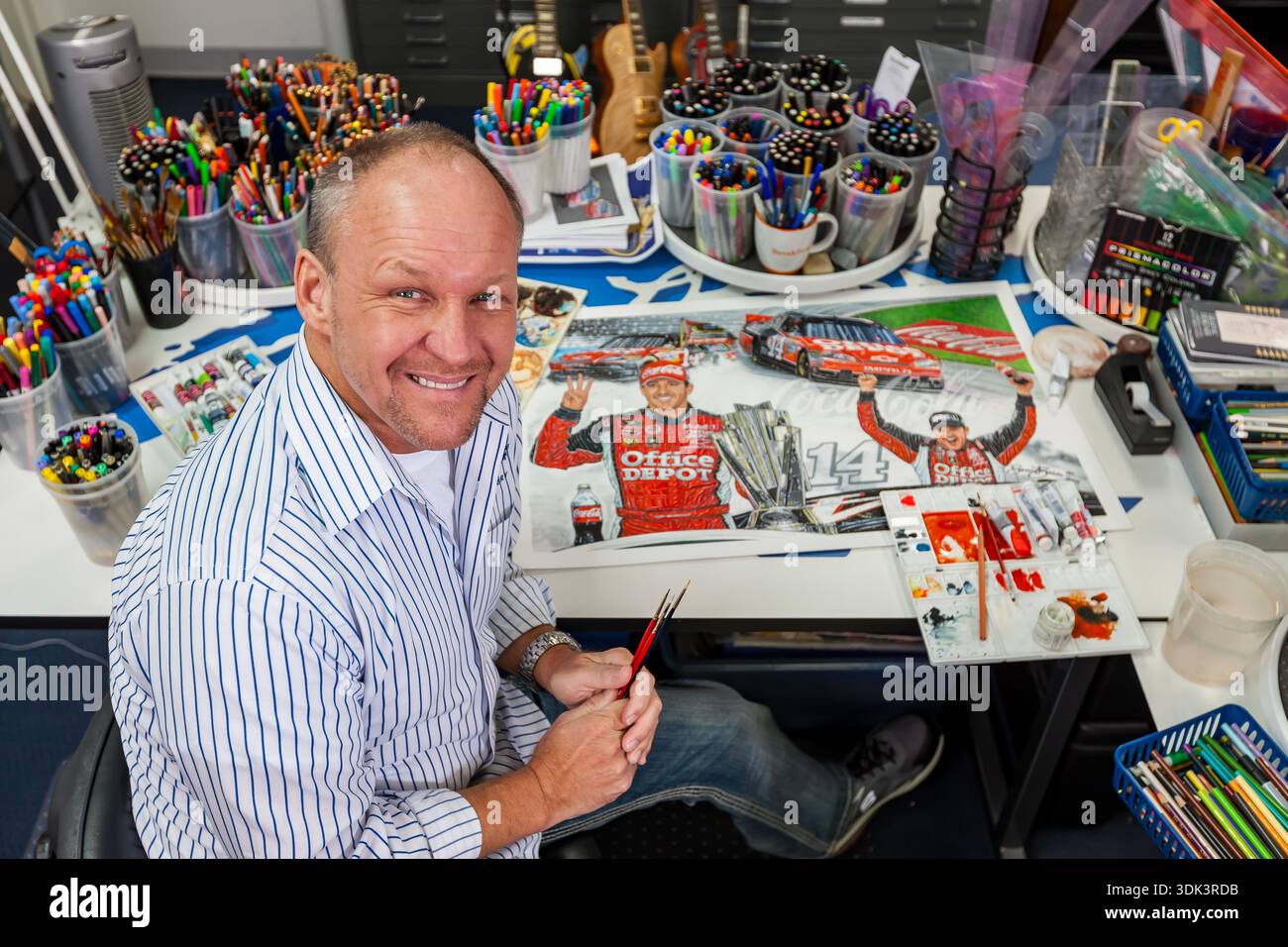 NASCAR artist Sam Bass stands proudly beside his vibrant artwork at his ...