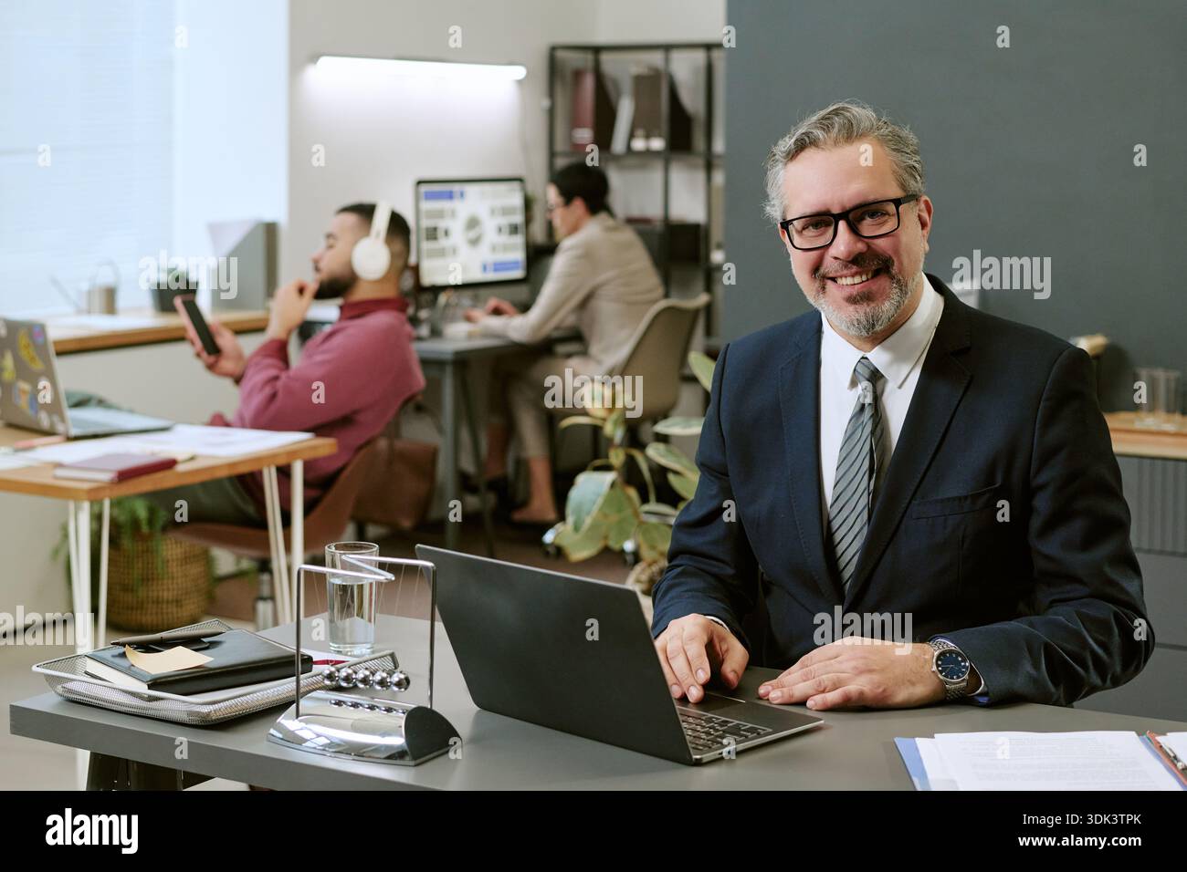 Middle Aged Man Smiling While Working on Laptop in Modern Office Stock Photo