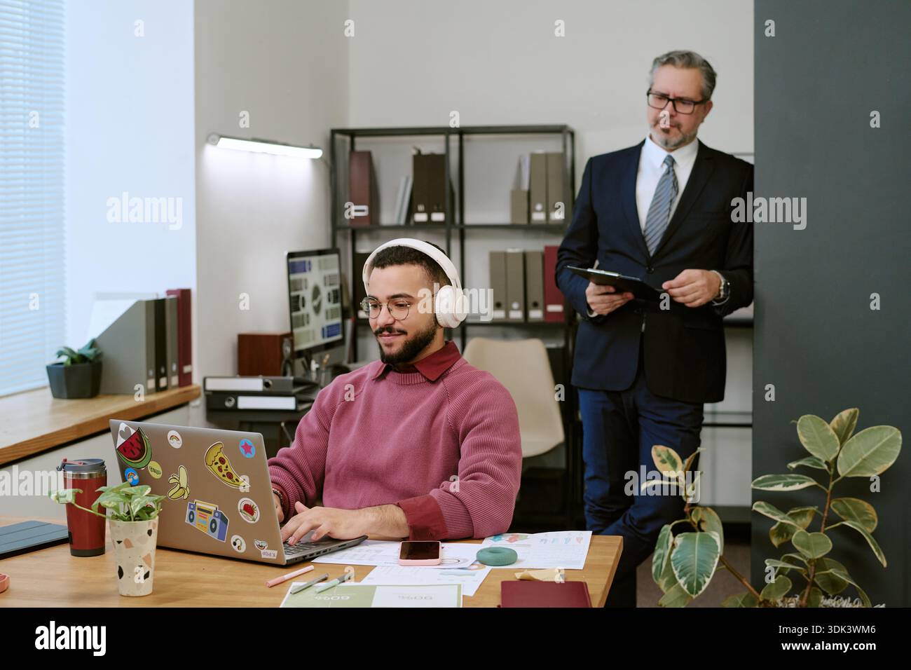 Young Adult Man Using Laptop While Middle Aged Man Observing Stock Photo
