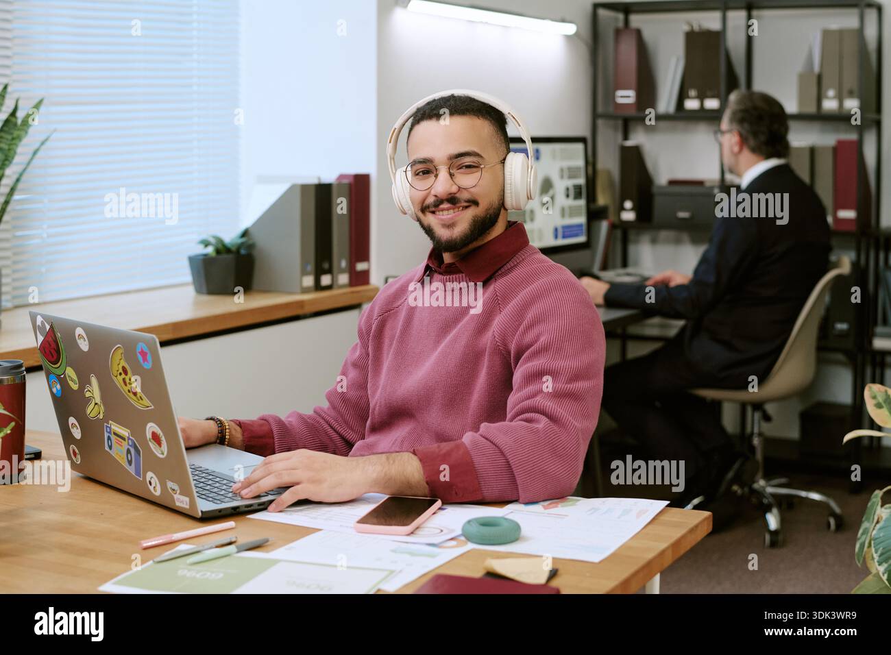 Young Adult Middle Eastern Man Smiling While Using Laptop in Modern Office Stock Photo
