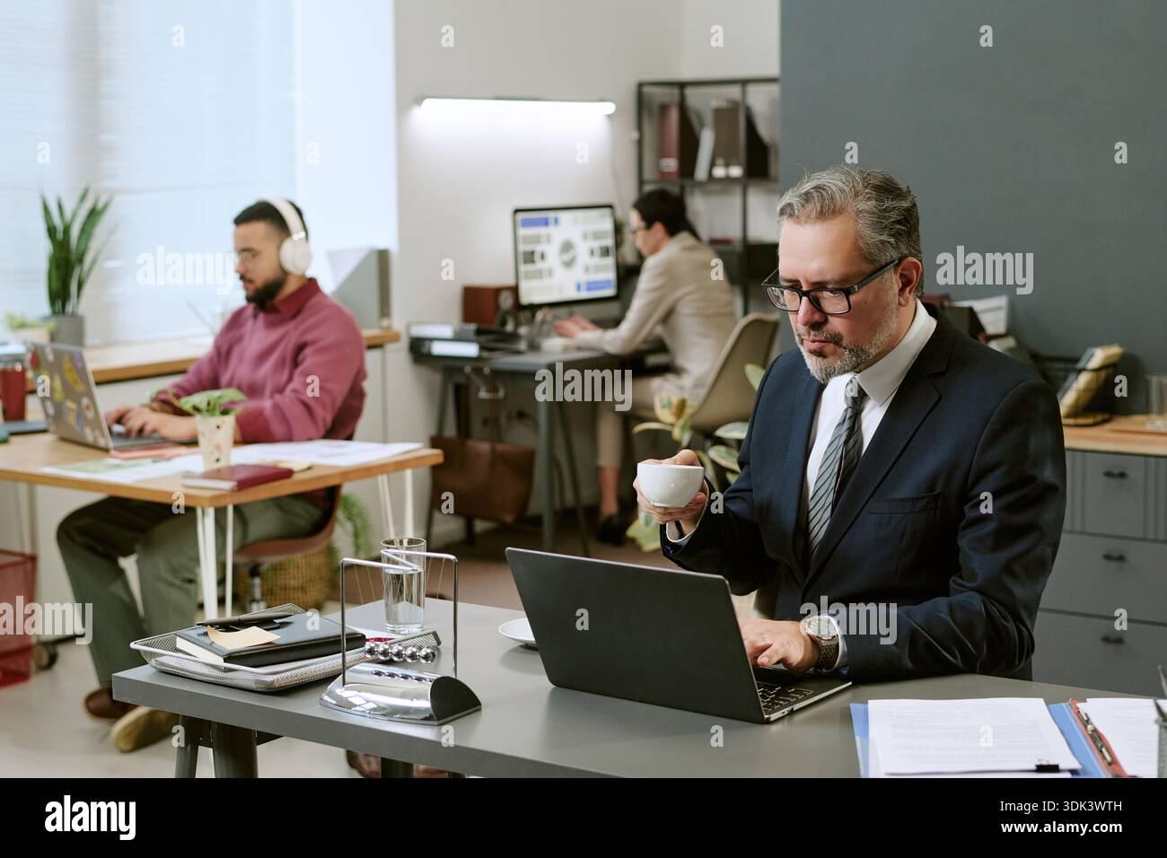 Middle Aged Man Working on Laptop While Drinking Coffee in Office Stock Photo