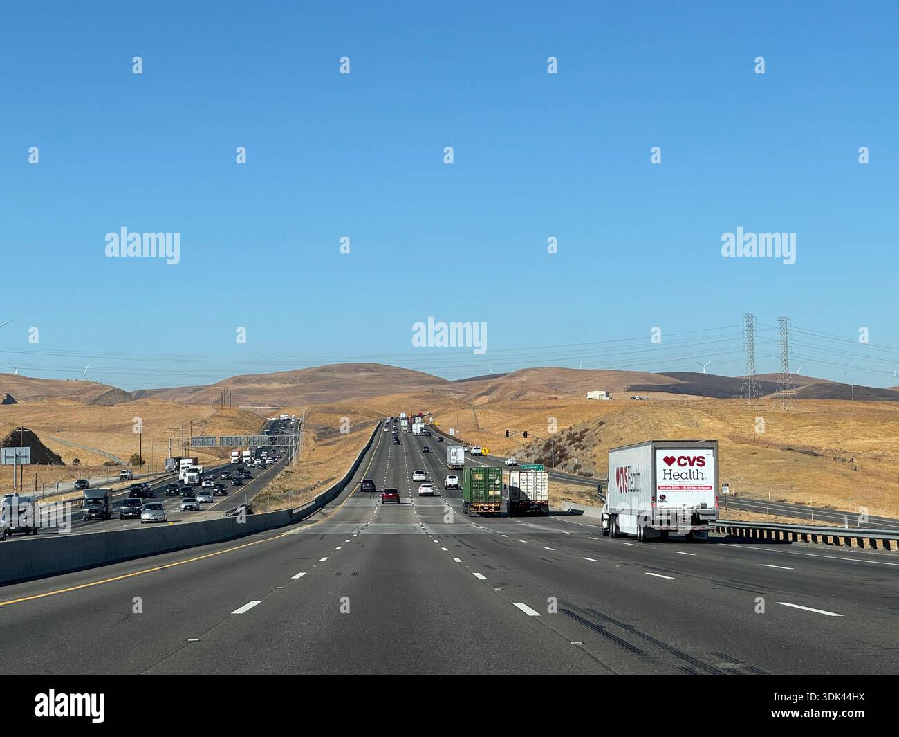 Multi-lane highway through dry California hills with heavy traffic and freight trucks under clear blue sky. - Smartphone Captured Stock Image