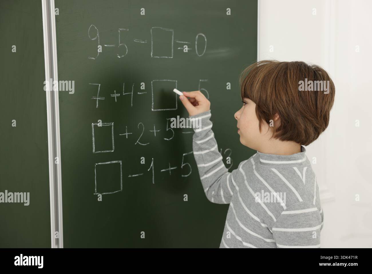 Schoolboy doing math on chalkboard in classroom Stock Photo