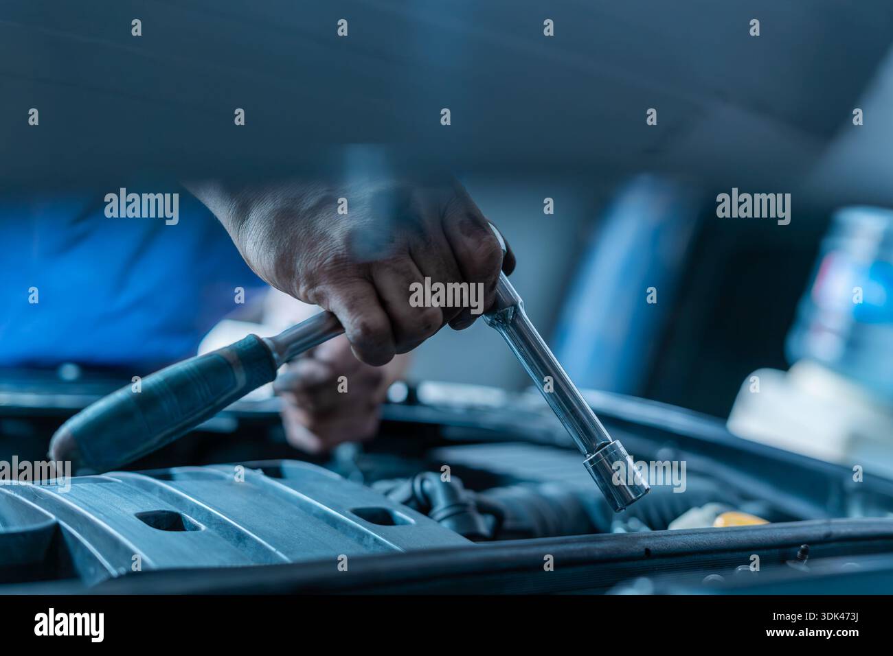Hand holding a socket wrench over a car engine Stock Photo