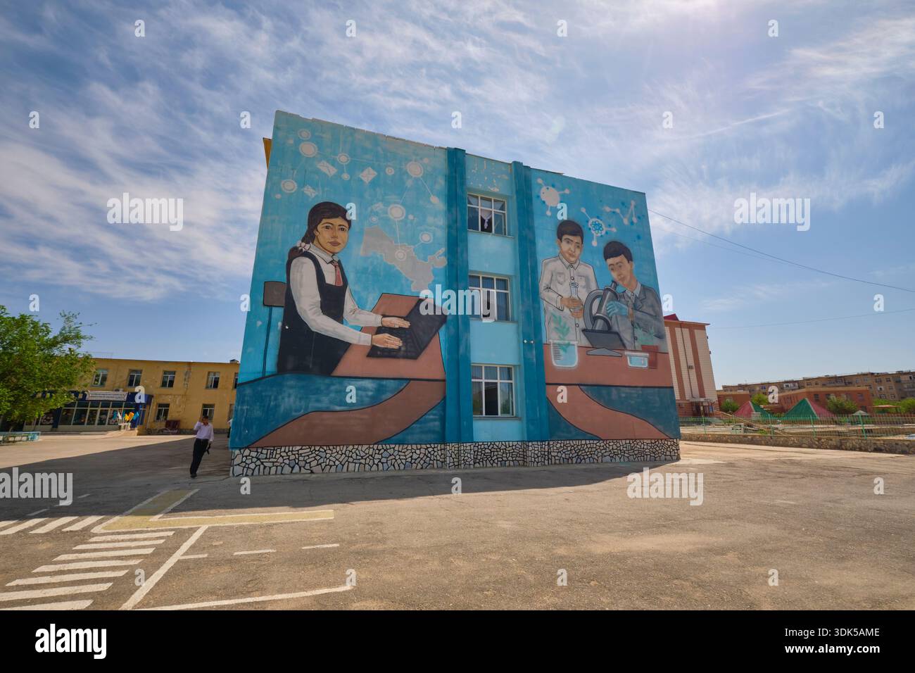 A large, colorful mural on the side of a school. Kids using a laptop, studying science. In Uchkuduk, Uzbekistan. Stock Photo