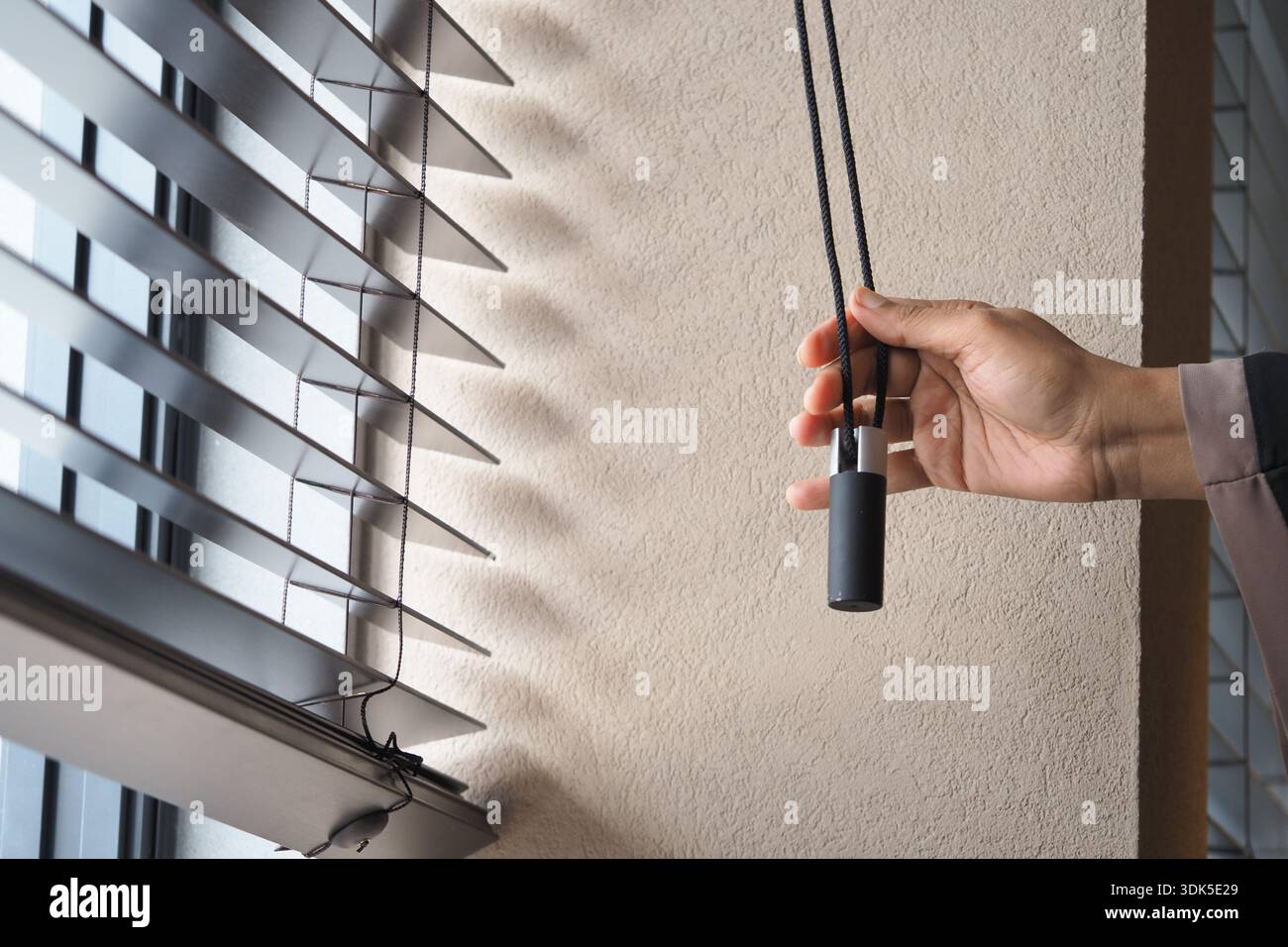 Pulling down window blinds in a bright room Stock Photo