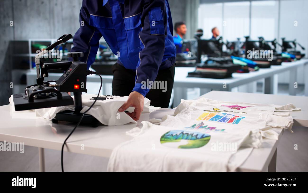 Young Hispanic Man Printing Custom T-shirts Using Heat Press Machine. Stock Photo