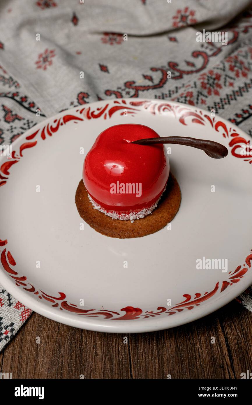 Red apple shaped cake with glossy icing on a white plate.A bright red mousse cake on a plate in a cozy interior Stock Photo