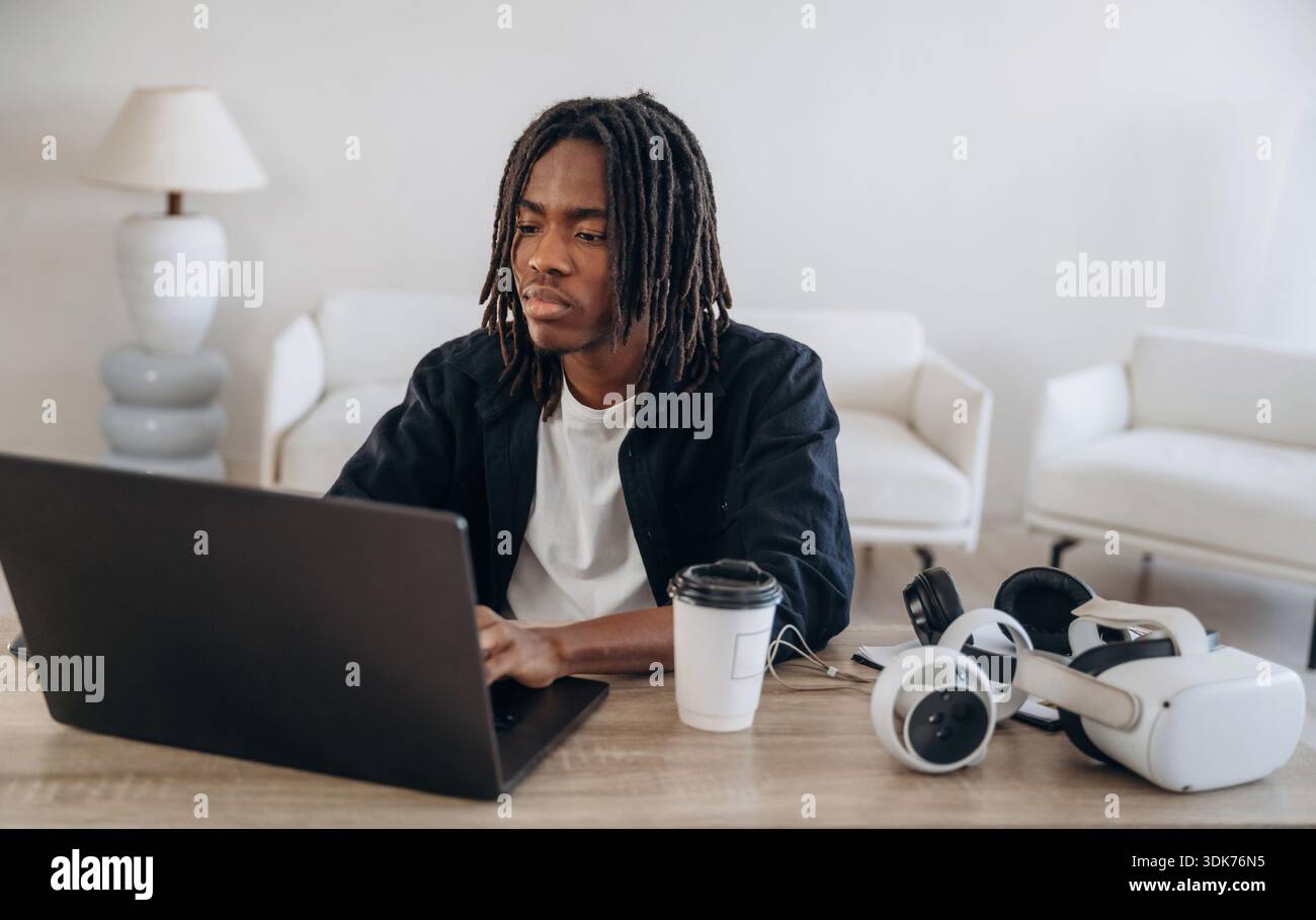Using computer. Young man is sitting by table with laptop and virtual reality glasses. Stock Photo