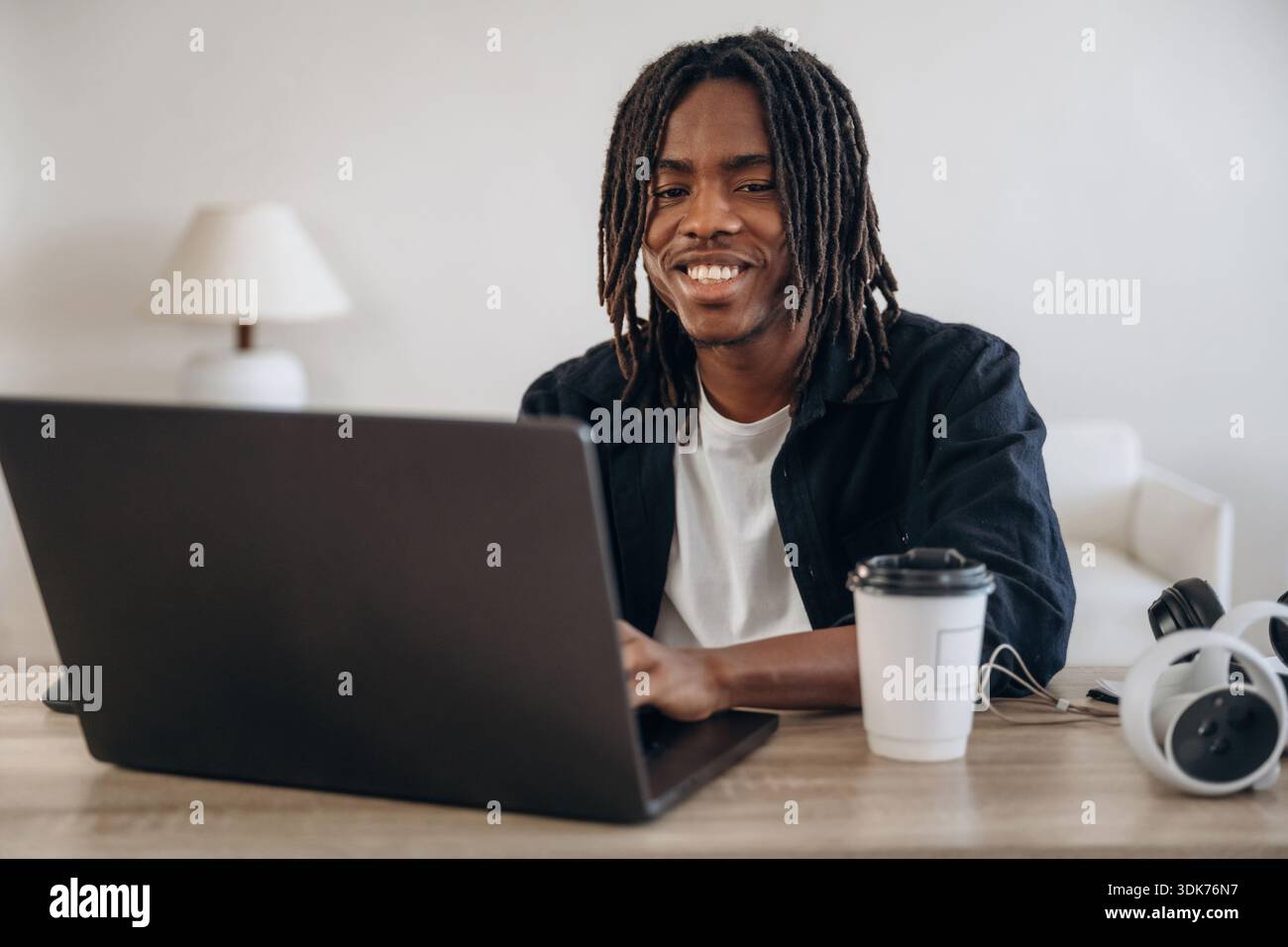 Young man is sitting by table with laptop and virtual reality glasses. Stock Photo