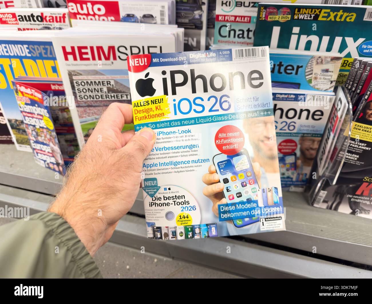 Berlin, Germany - Sep 25, 2025: Man hand holds German tech magazine iPhone 26 new designs iOS26 Apple Intelligence kiosk rack Auto Kauf Linux Spiegel Stock Photo