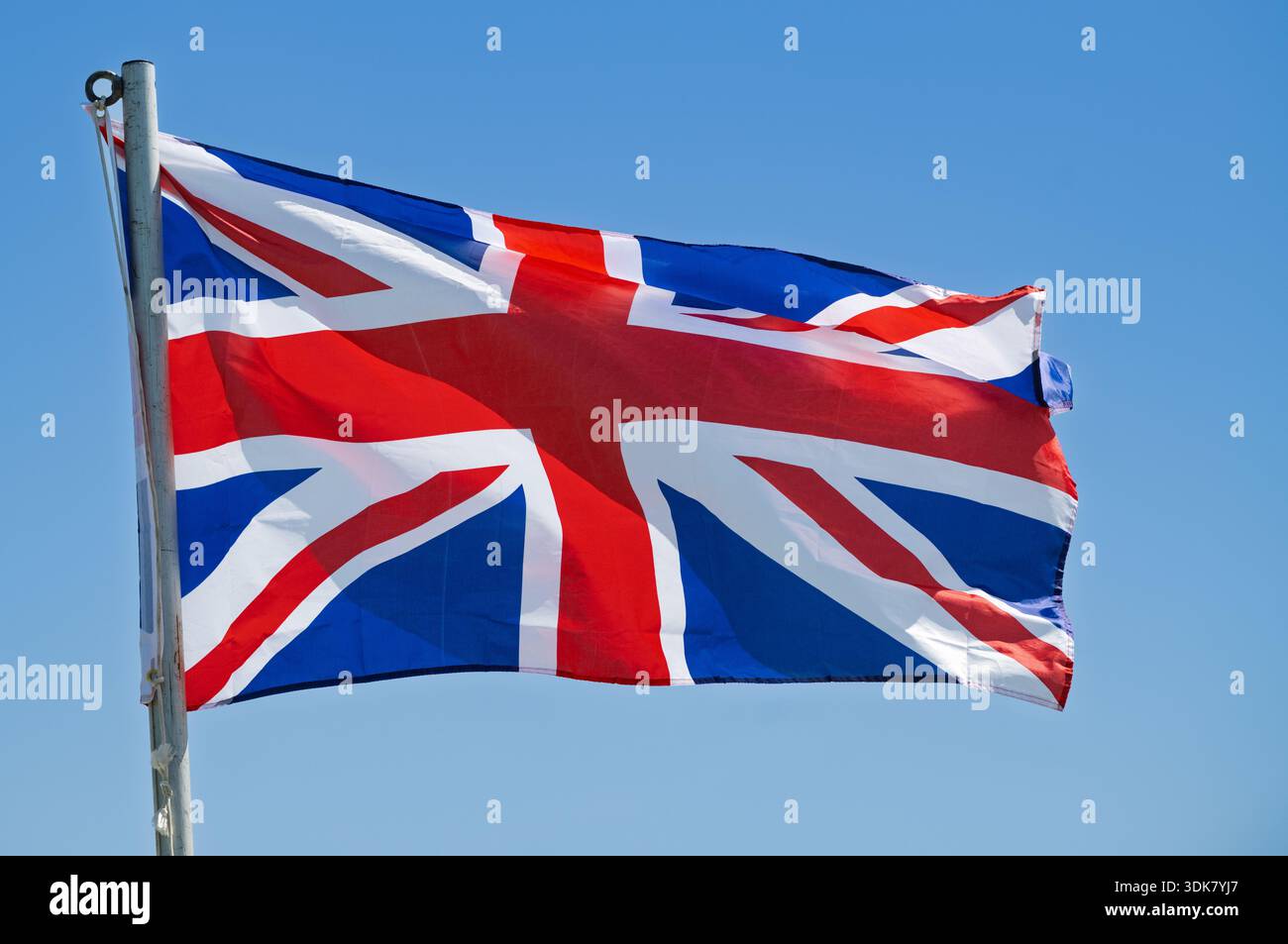 Union Jack flag blowing in the wind against a clear blue sky ...