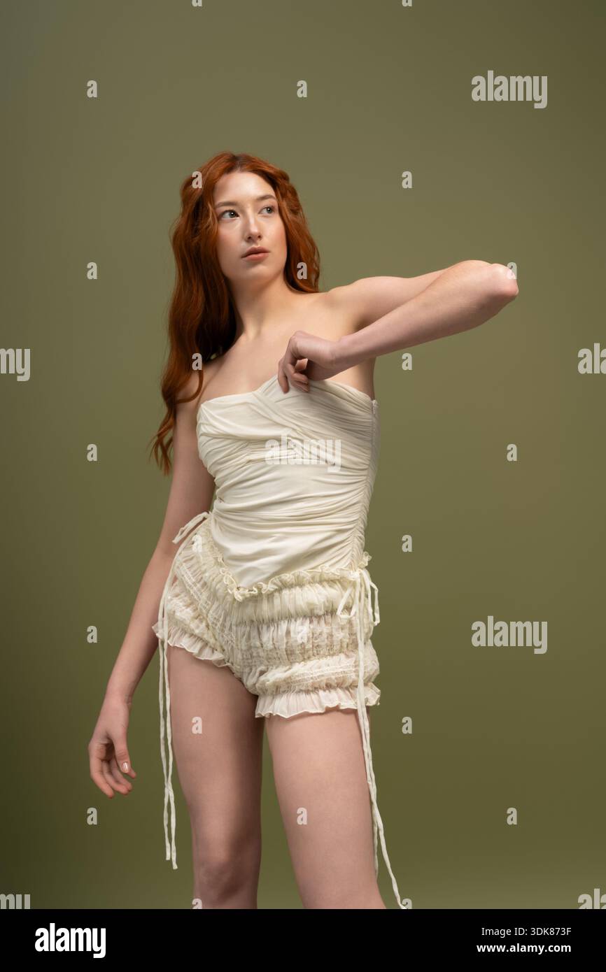 A red-haired young woman models stylish spring attire in a studio, radiating elegance. Stock Photo