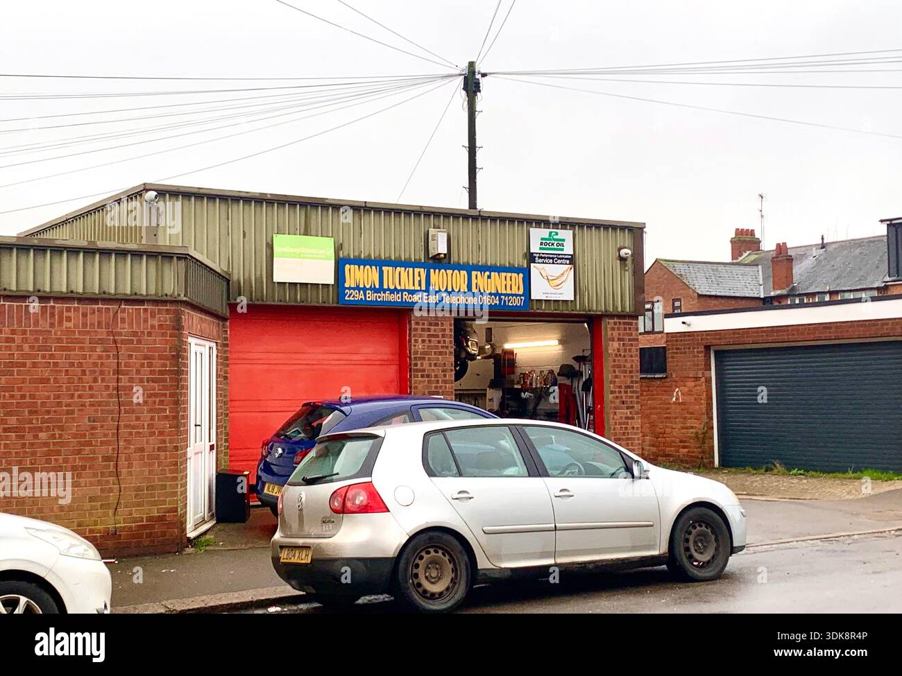 Independent motor engineering garage with vehicles parked outside as mechanics work inside the workshop an RAC approved service centre UK - Smartphone Captured Stock Image