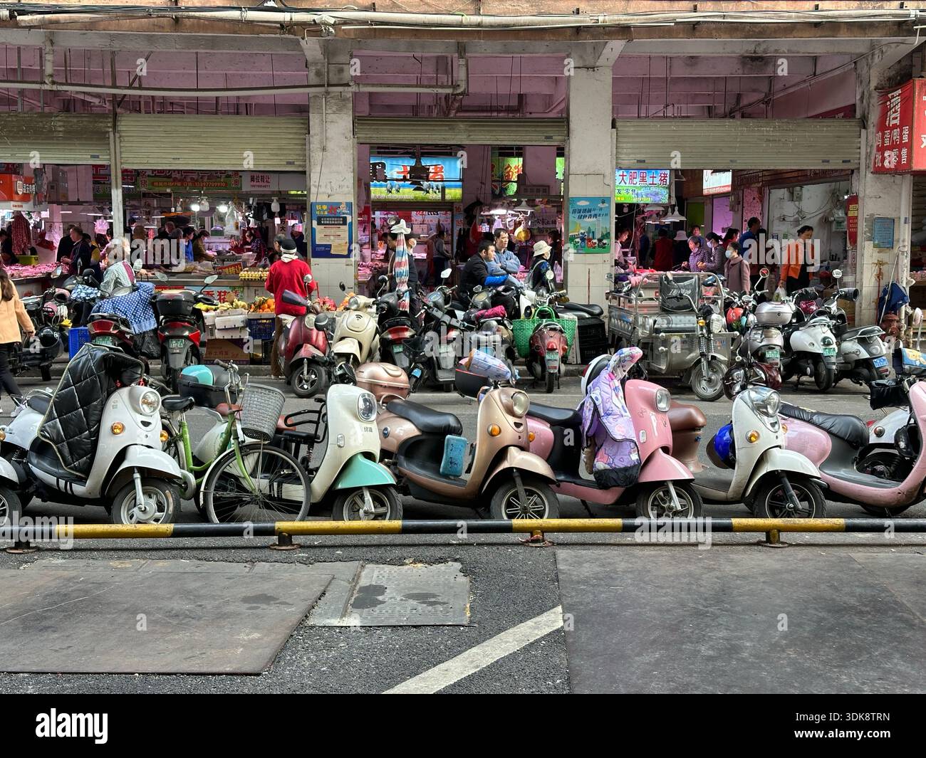 Nanning, China - Jan 7, 2024: Busy street market scene with many parked scooters and people shopping in China. - Smartphone Captured Stock Image