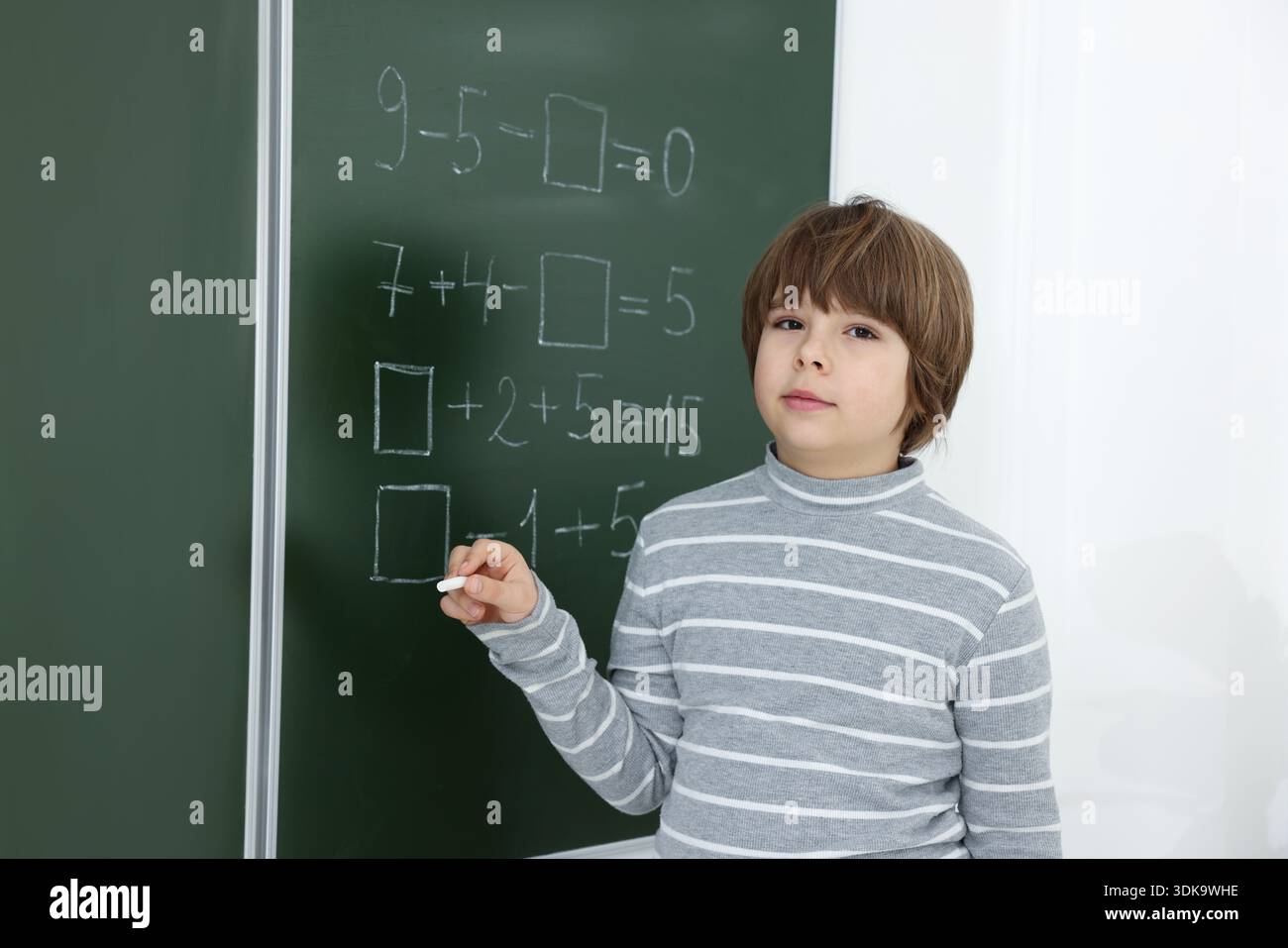 Schoolboy doing math on chalkboard in classroom Stock Photo