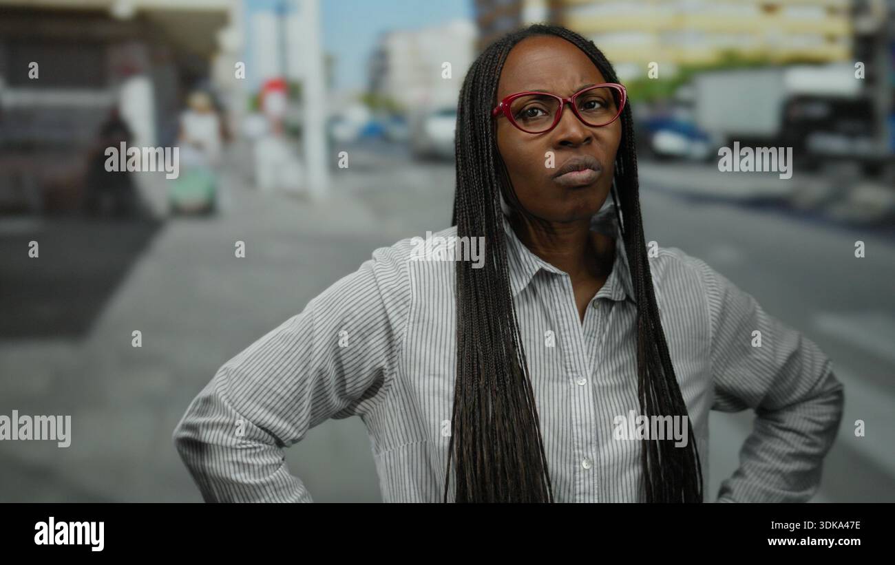 Woman with curly hair stands outdoors on a city street with arms ...
