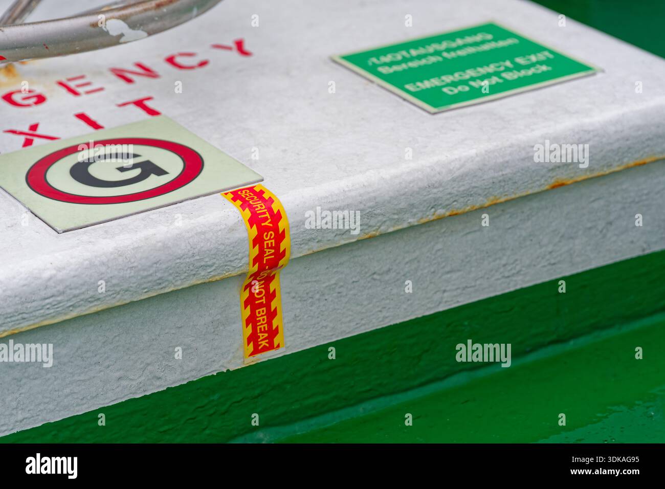 A metal emergency exit cover shows warning labels and intact seal tape ...