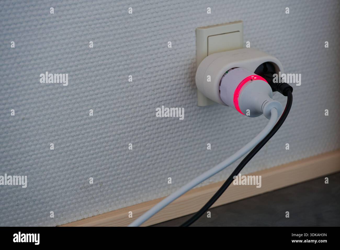 Smart power plug with glowing red indicator connected to wall socket ...