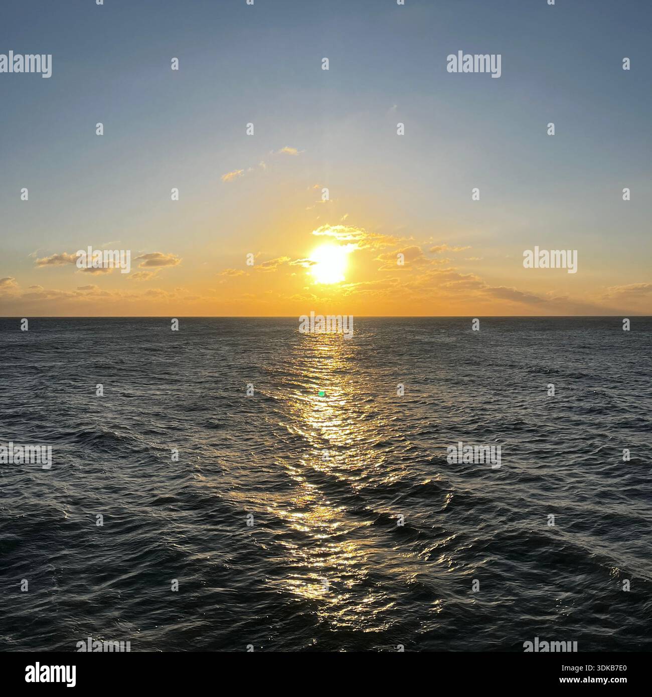 Golden sunset reflecting across the surface of the ocean with gentle waves and clear horizon, calm and peaceful seascape background - Smartphone Captured Stock Image