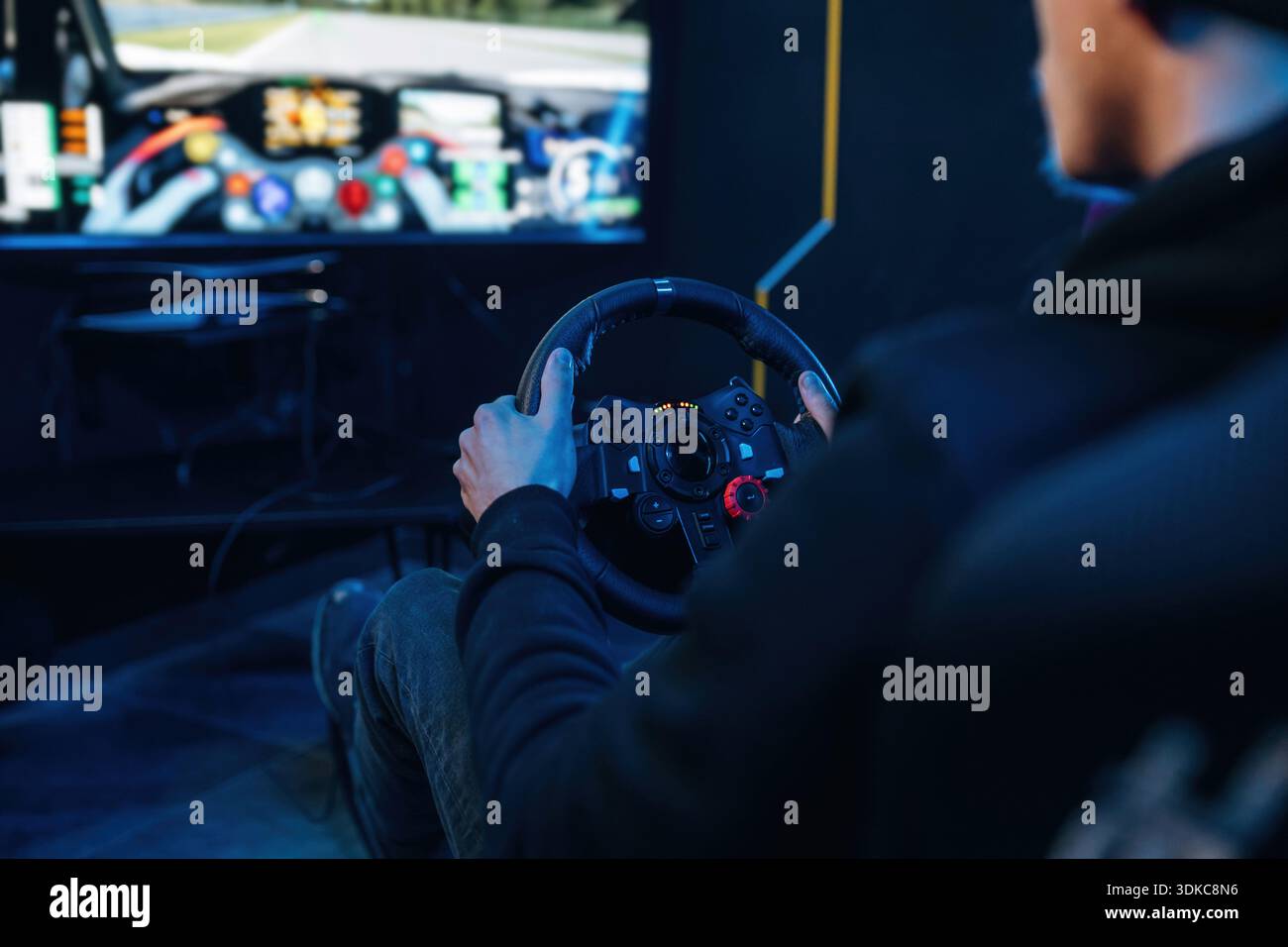 Using steering wheel. Young guy is playing racing game by using driving simulator. Stock Photo