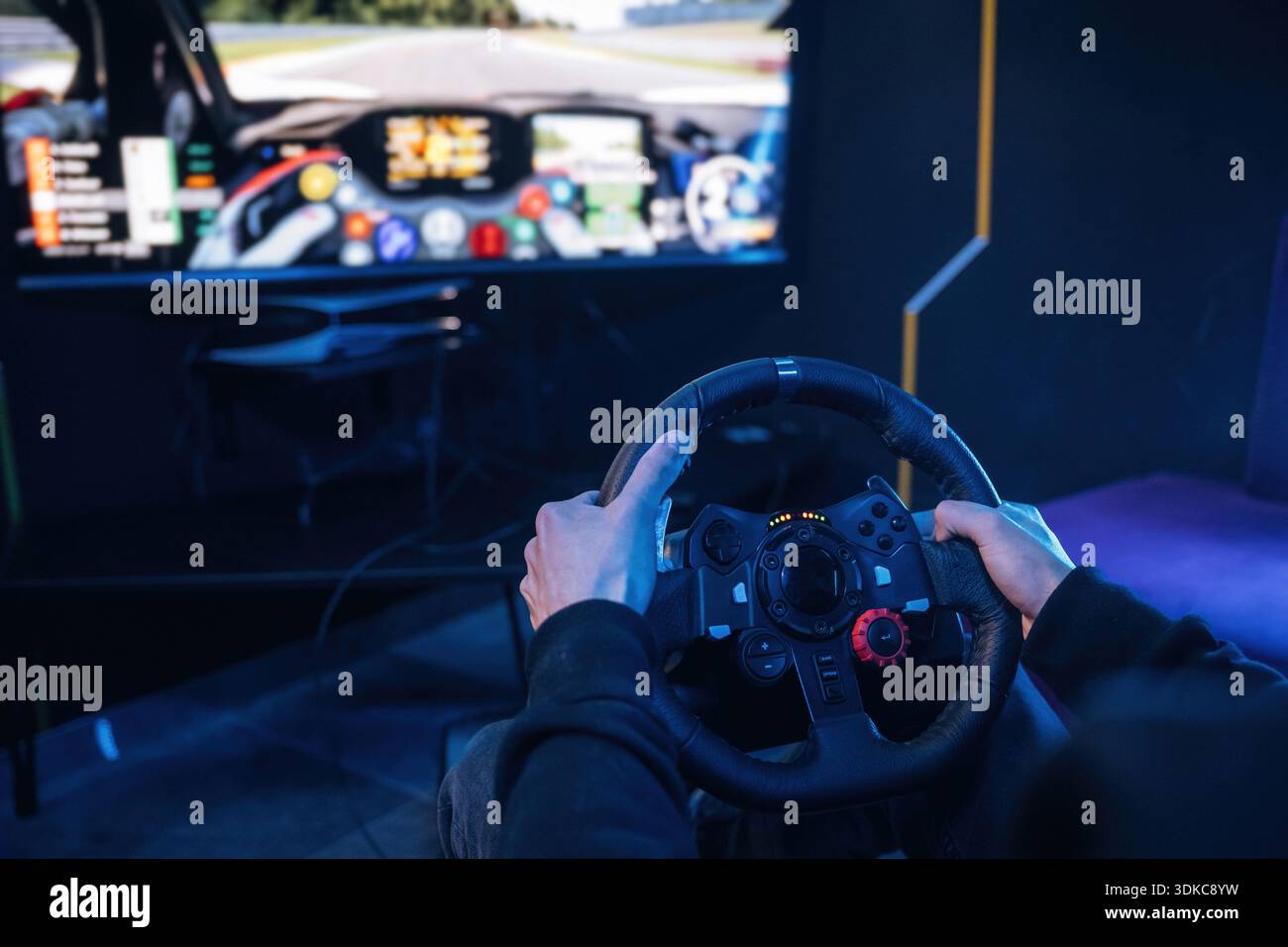Using steering wheel. Young guy is playing racing game by using driving simulator. Stock Photo