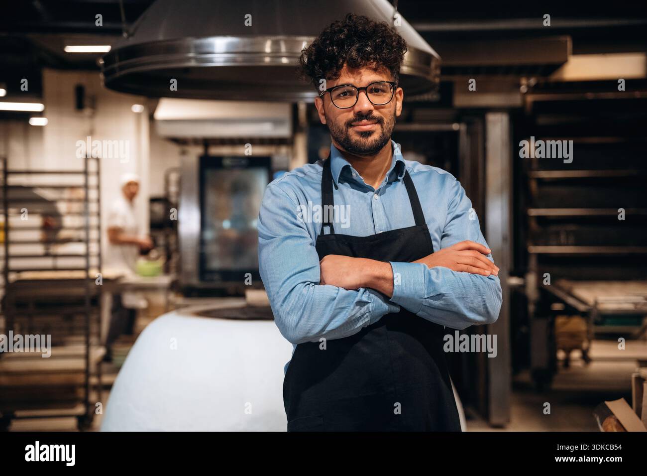 Bakery worker in apron is standing indoors. Stock Photo