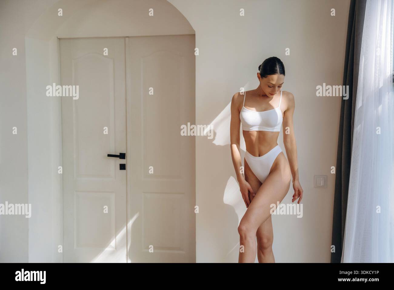 Beautiful woman is standing and posing. Young female in fitness clothes is in the room. Stock Photo