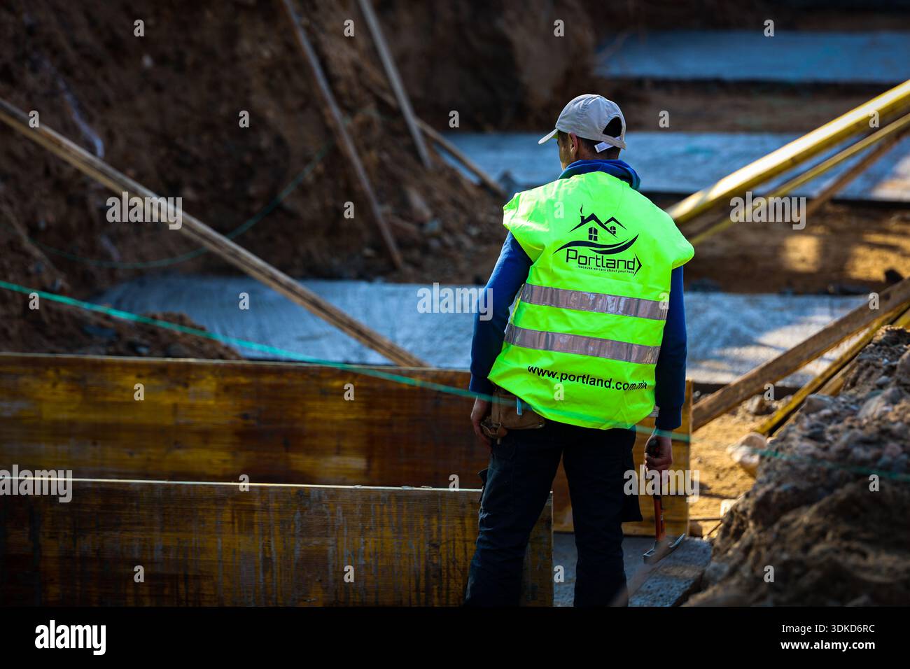 Construction worker holding a hammer while inspecting timber formwork and concrete foundations at an active building site Stock Photo