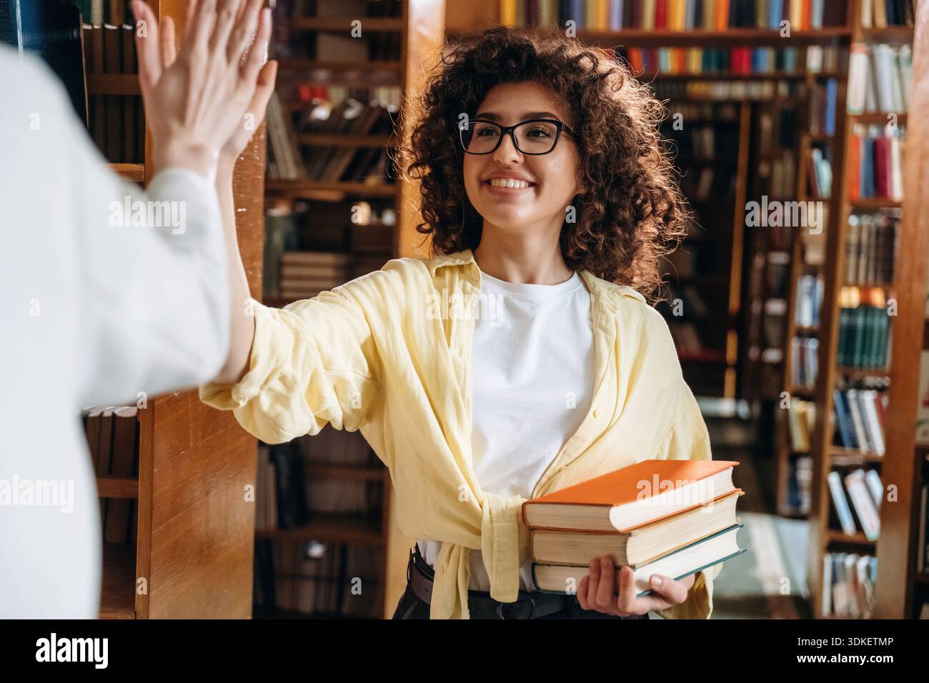 Two women are doing high five in the library. Stock Photo
