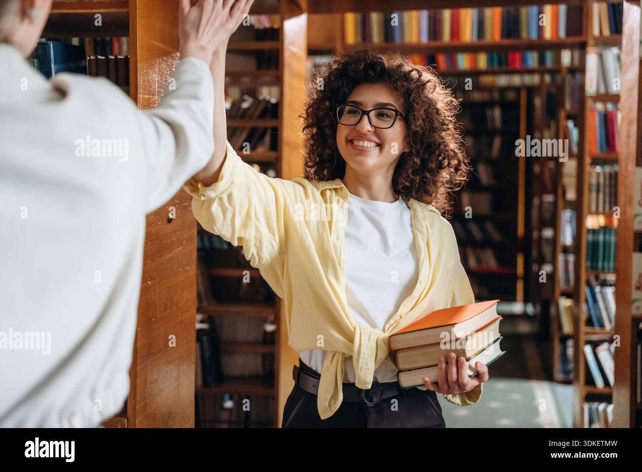 Two women are doing high five in the library. Stock Photo