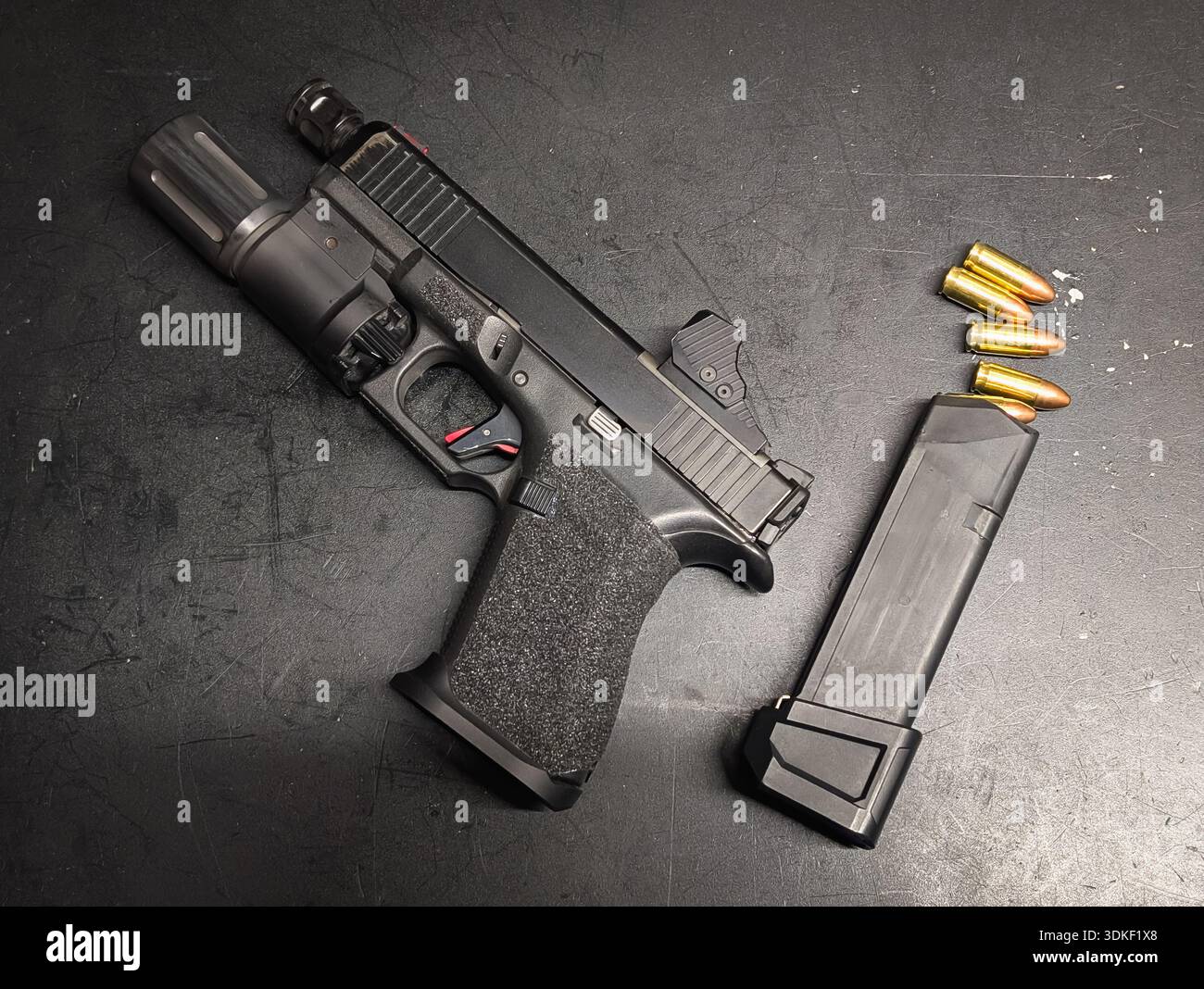 Modern semi-automatic black handgun with tactical flashlight, optical sight, extended magazine and ammunition on dark textured background for defense Stock Photo