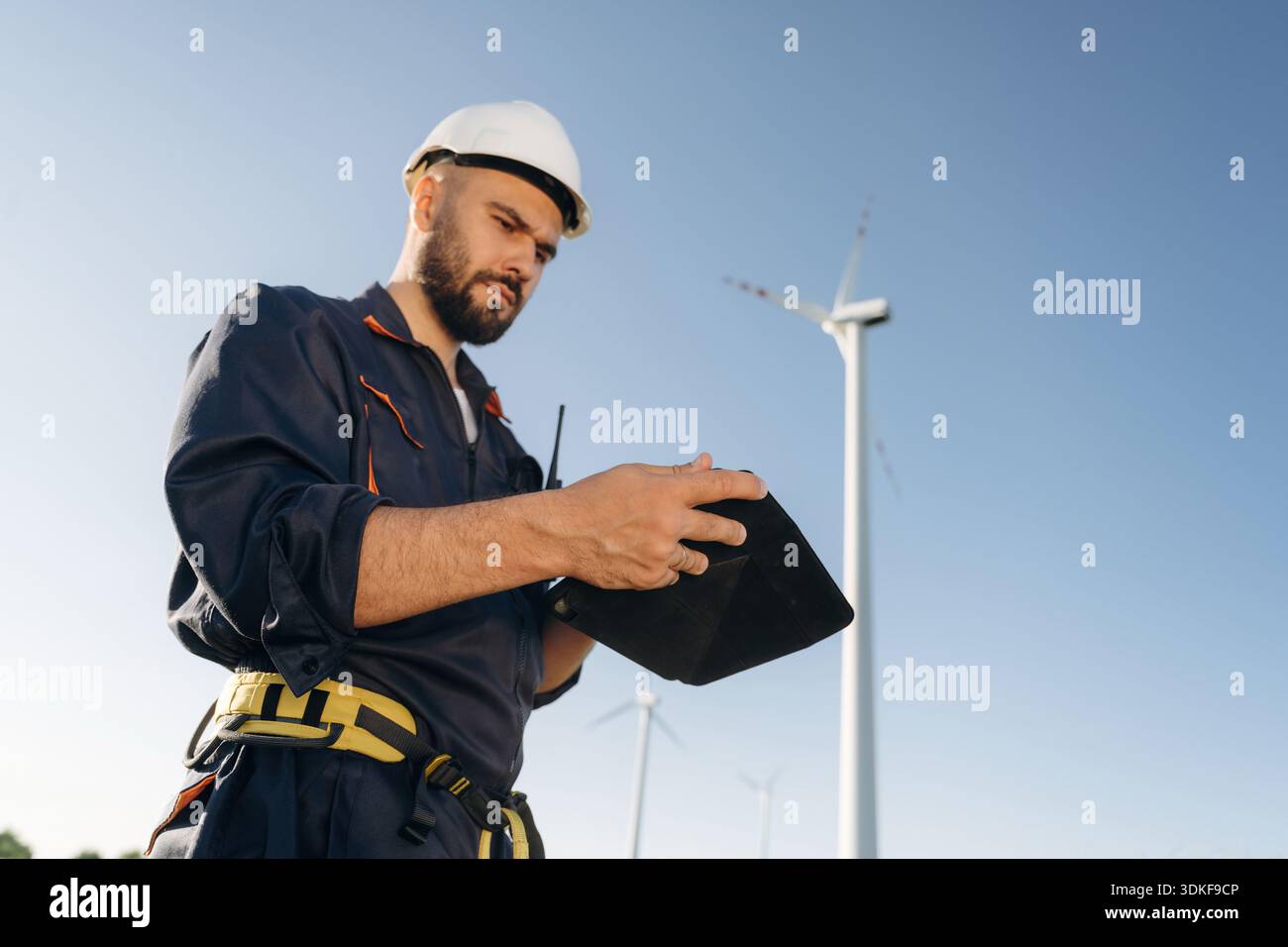 Reading information on digital tablet. Engineer in field checking on wind turbine production. Stock Photo