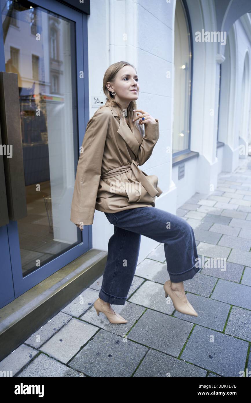 Designer woman in a trench coat and jeans poses confidently on an urban ...