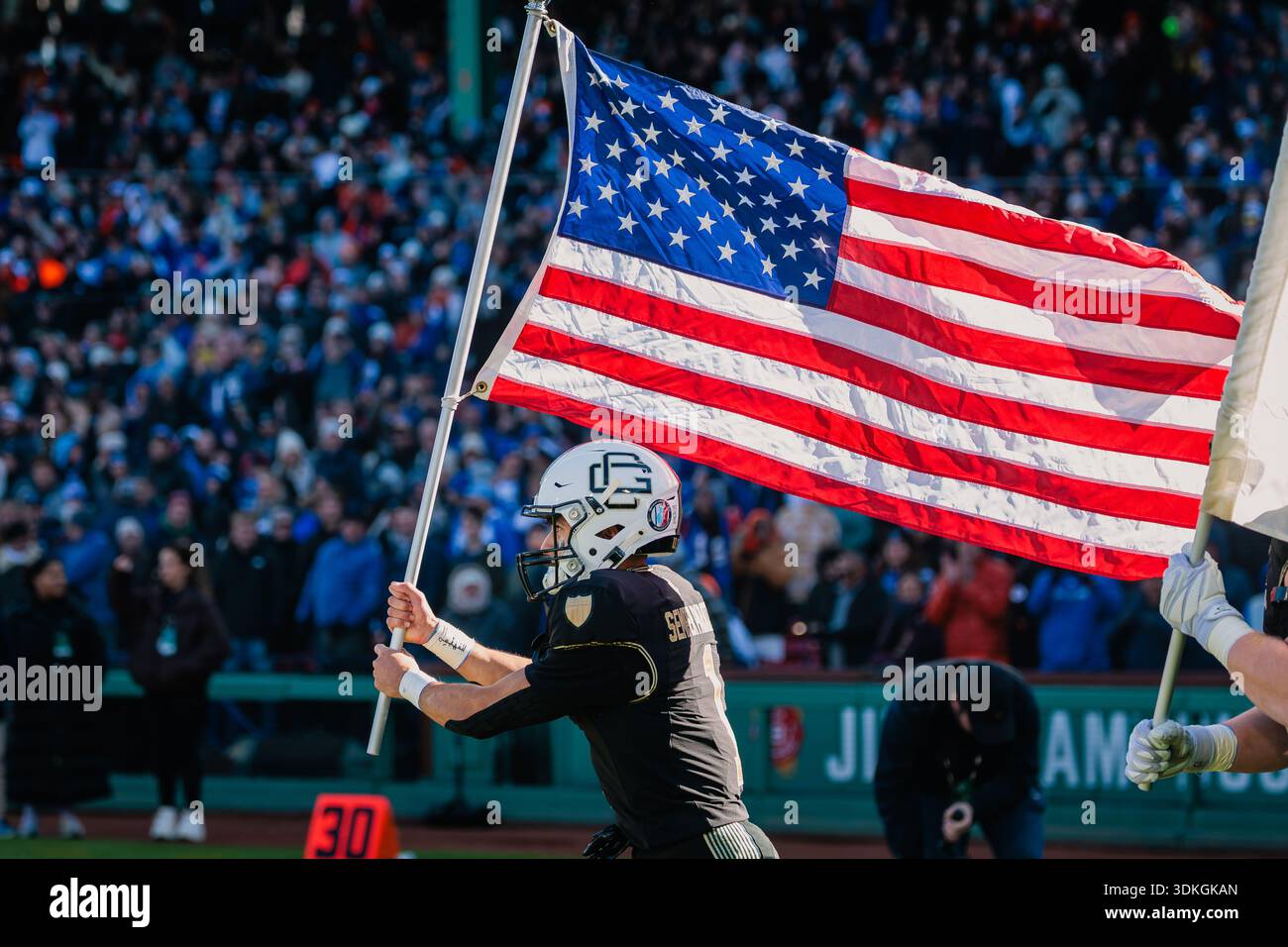 A Coast Guard football player carries the American flag onto the field ...