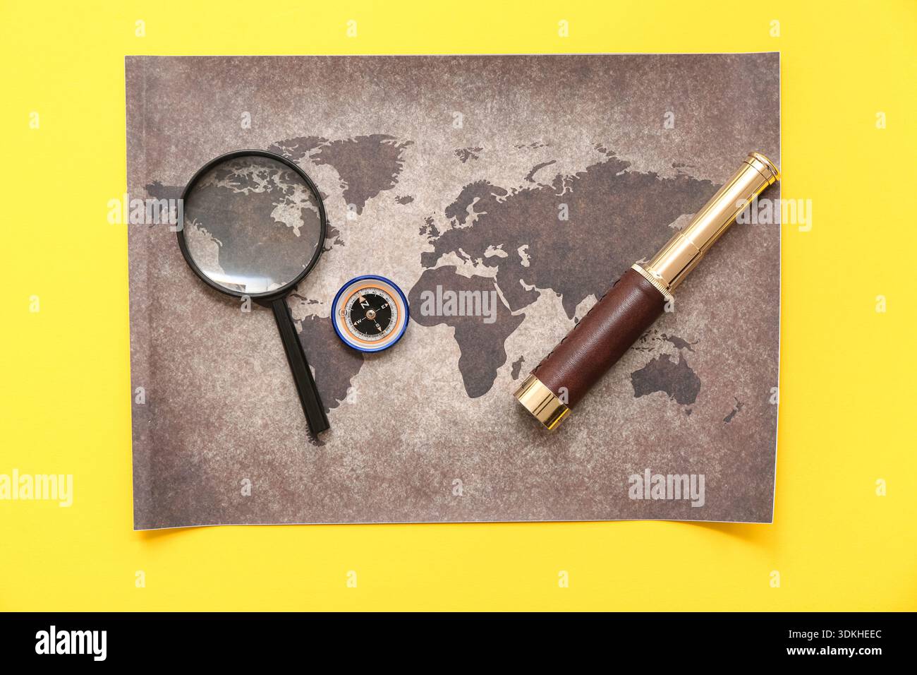 Composition with modern compass, world map and magnifier on yellow background Stock Photo
