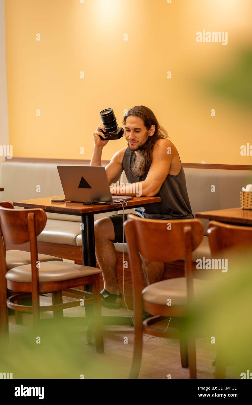 Male photographer working on laptop holding camera in cafe Stock Photo