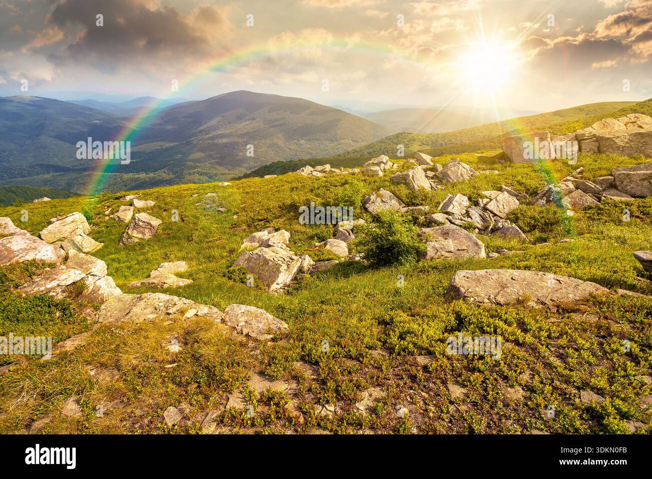 mountain landscape in summer with rocks at sunset. green grass under blue sky in dramatic evening light. alpine meadow and rolling hills with boulders Stock Photo