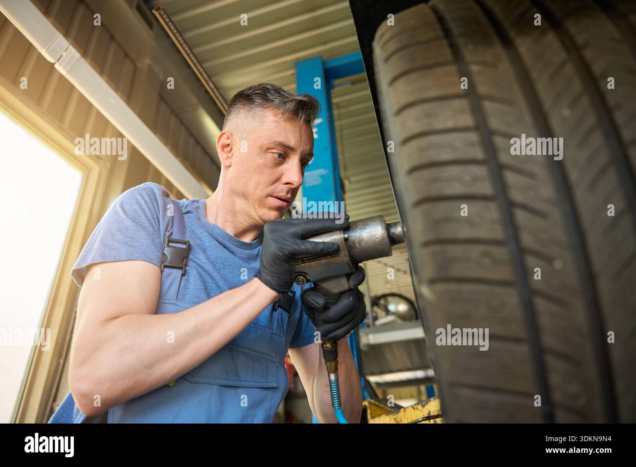 Mechanic holds a removed wheel in front of him Stock Photo - Alamy