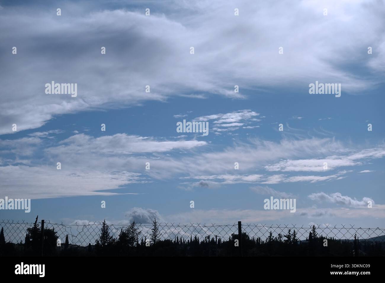 Fence and tree silhouettes under cloudy blue sky. Stock Photo